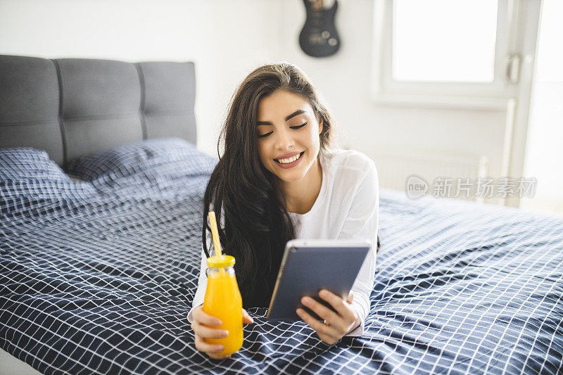 快乐的女人看报纸，喝果汁，早上躺在床上