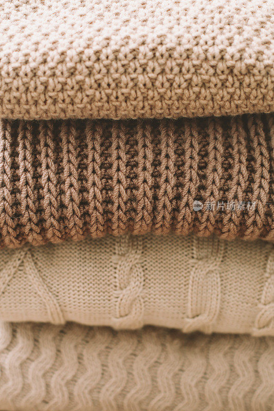 在浅色背景上的一堆毛格子呢。分层排列的不同图案的机织物针织衣服(毛衣、围巾、套头毛衣)。