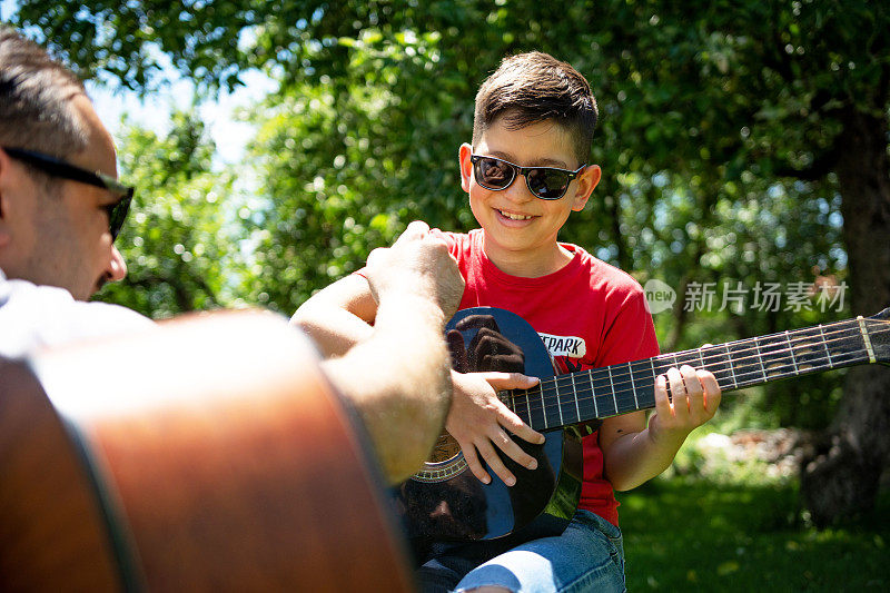 一个男孩跟他父亲学弹吉他的照片