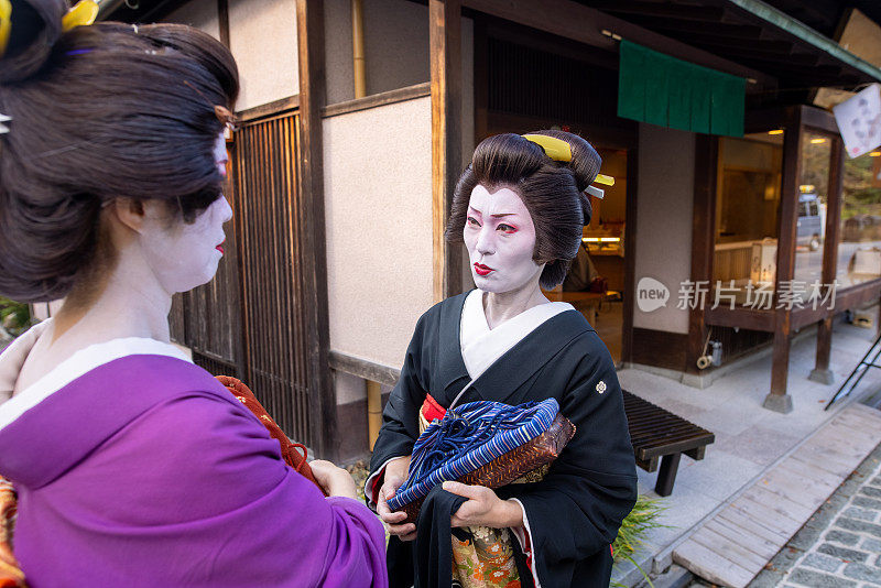 在京都祗园的传统日本街道上，两名艺妓在交谈