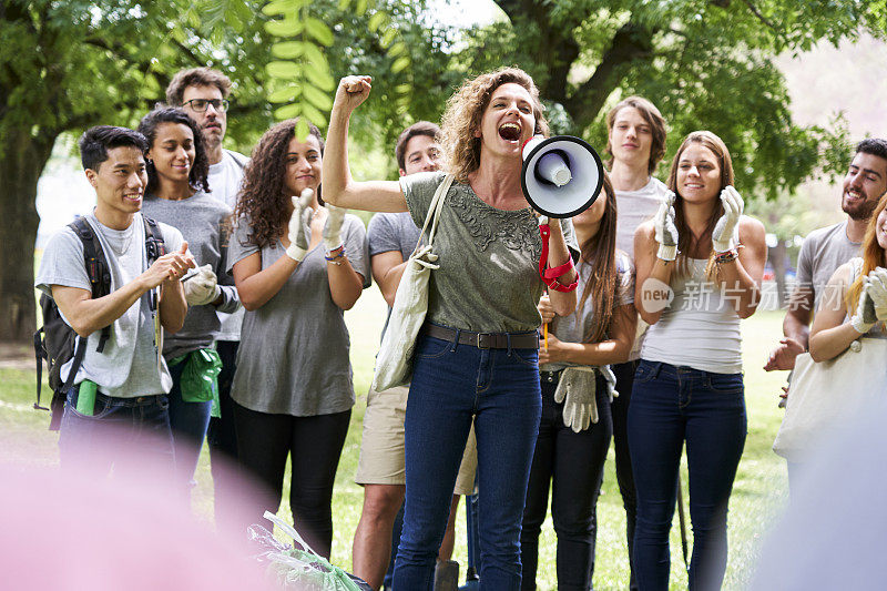 在公园里，站在一群志愿者前面的女性活动家用扩音器讲话