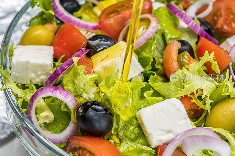 在新鲜蔬菜沙拉中加入橄榄油的特写。