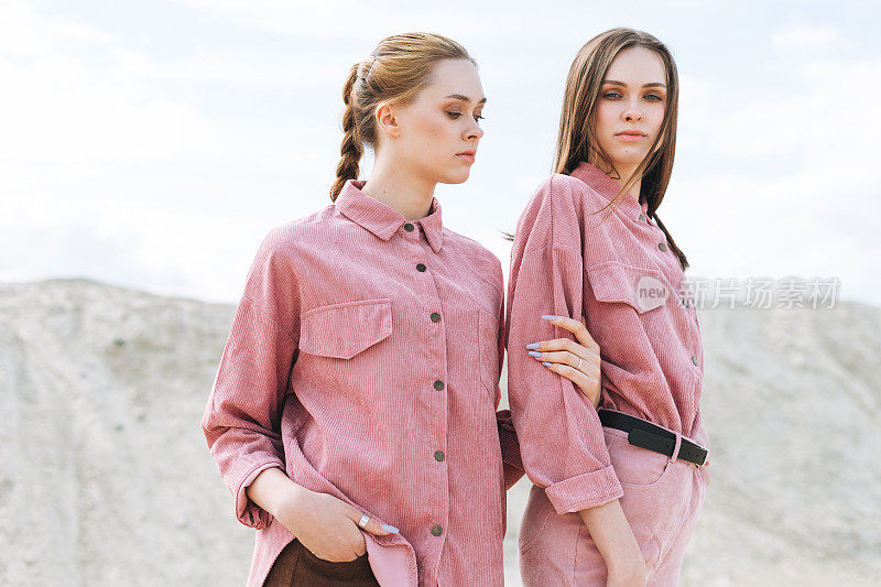 时尚美女肖像年轻女子姐妹在沙漠的背景粉红色有机天鹅绒衬衫