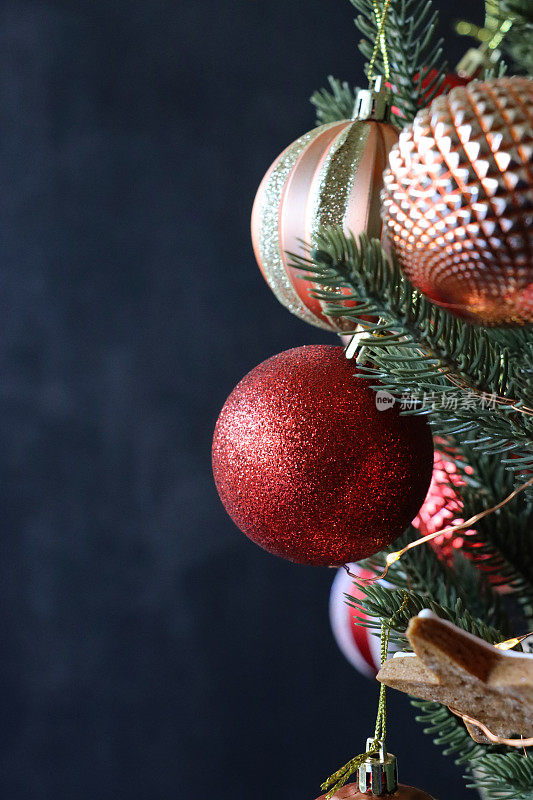 形象的个人，红色闪光和铜纹理的小装饰物挂在人造圣诞树的树枝上，云杉针，模糊的白色神仙灯的背景，复制空间