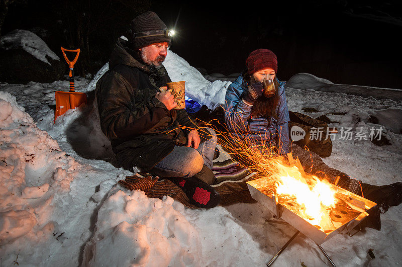 一对夫妇在他们的雪营地放松，享受饮料