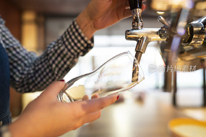 一个辨认不出的酒保手在啤酒龙头向玻璃杯中倒入散装啤酒的特写