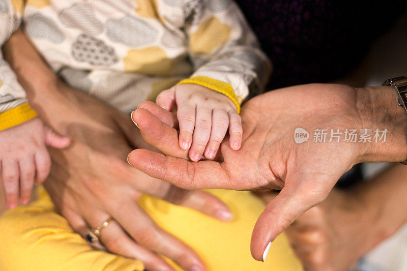 小婴儿的手放在成年女性的手上，人类的手在对比的光线下细节，母亲用可爱的小手指握着小婴儿的手