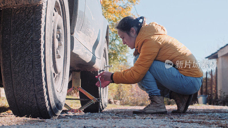 一位妇女在乡村公路上给汽车换轮胎。DIY