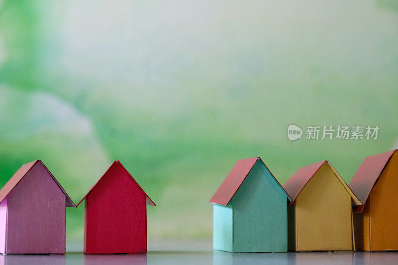 特写图像的多色纸板房子，彩色的海滩小屋，重点在前景，斑斑驳杂的绿色背景，家庭财务，房地产和假日储蓄概念
