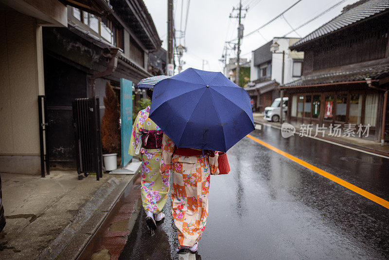 女性朋友穿着和服在雨天走在传统的日本村庄