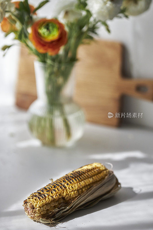 烤玉米，花和花瓶放在阳光下的桌子上