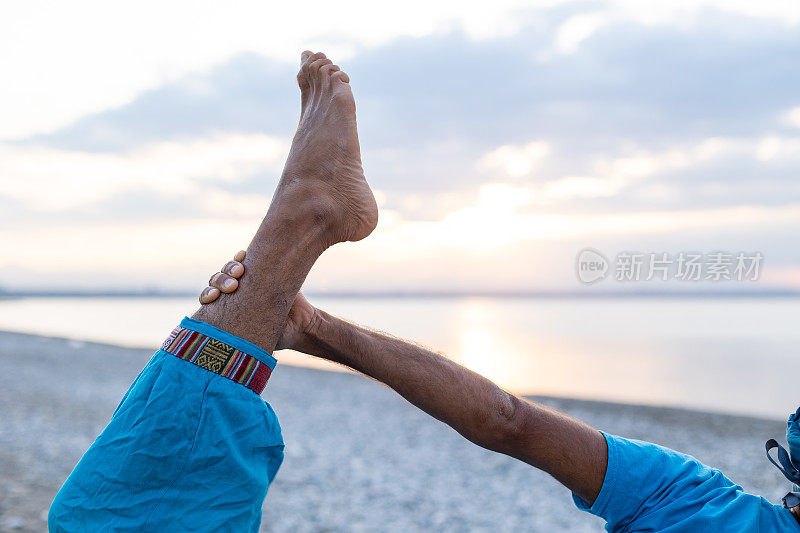 在日出或日落的时候，健康的年轻人在平静的海边练习瑜伽