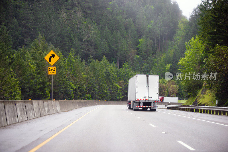 两辆带拖车的半挂车在分隔的高速公路的转弯处互相移动