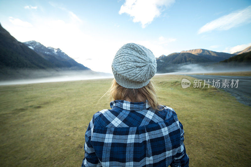 年轻女子站在雾蒙蒙的草地上凝视着风景