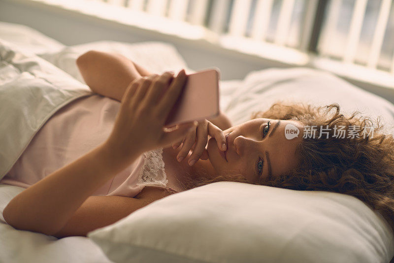 年轻漂亮的女人在床上玩手机