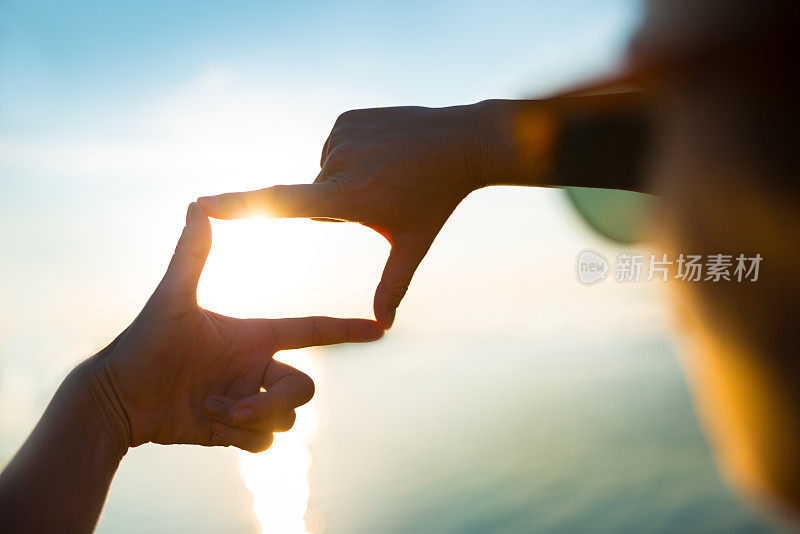 幸福的女人捕捉日落的水-手指框架