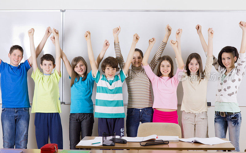 快乐的十多岁的学生举起手站在白板旁边。