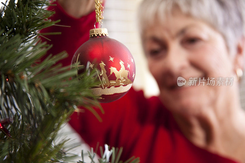 老妇人将圣诞装饰品挂在XXXL圣诞树上