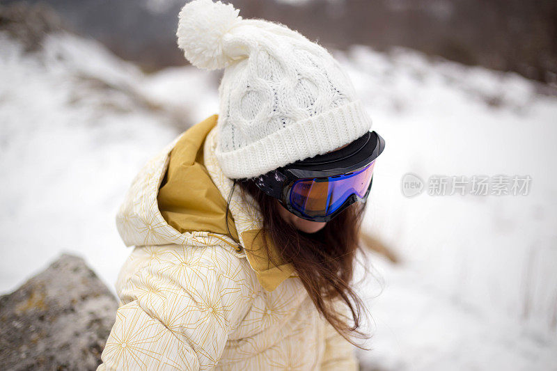 女人拿着滑雪板，背景是高山