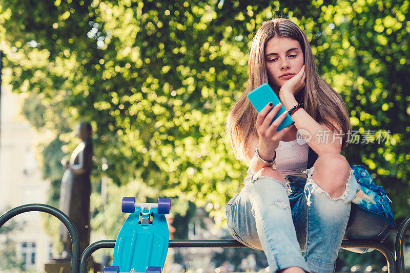 女孩用滑板在城市公园发短信