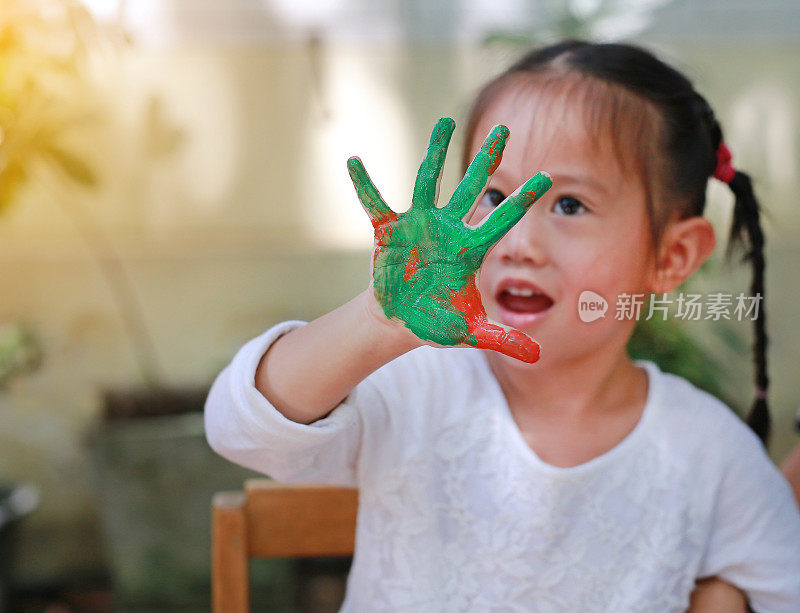 可爱的小女孩，画着绿橙色的手在公园里，专注于她的手。
