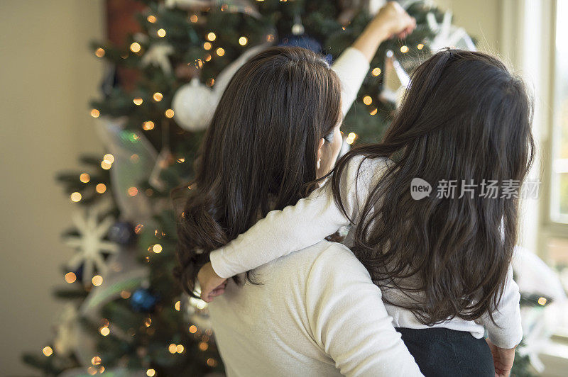 一位母亲和她蹒跚学步的女儿在装饰圣诞树