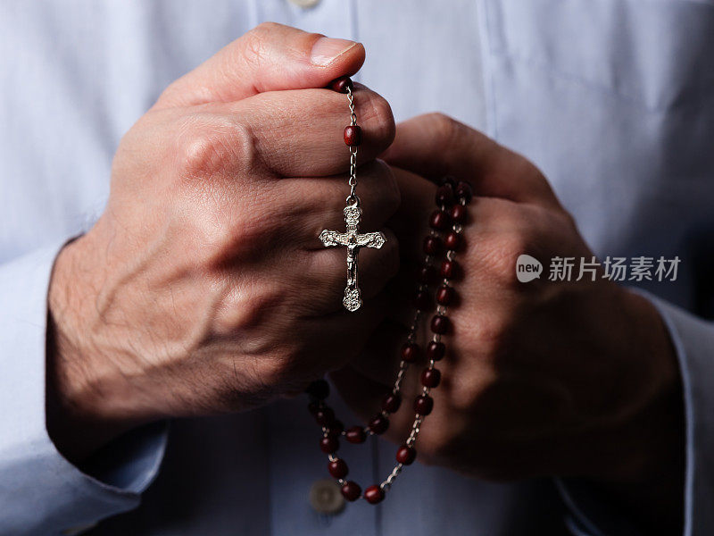 男性手握念珠祈祷，念珠上有耶稣基督在十字架或十字架上的黑色背景。