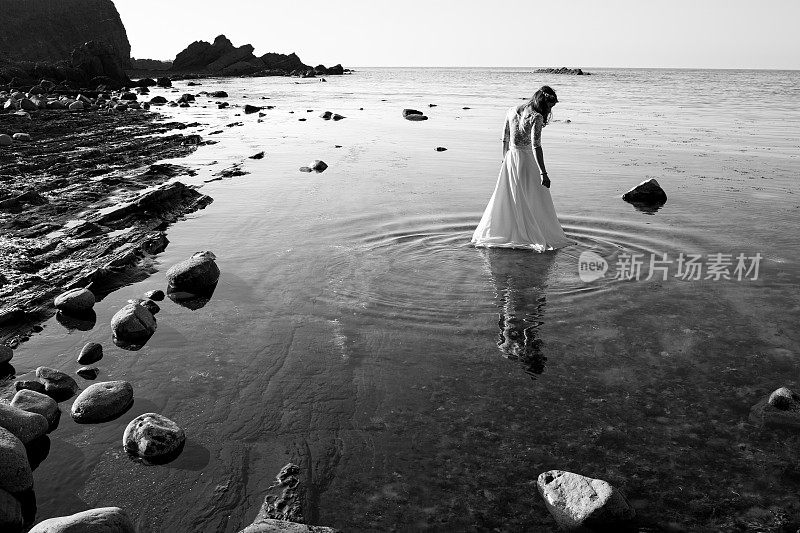 年轻的新娘在美丽的海岸线上步入水中