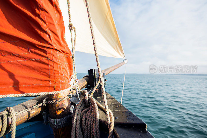缠绕在木夹板上的绳子固定在一艘有米色三角帆和赭色帆的老式帆船的船体上