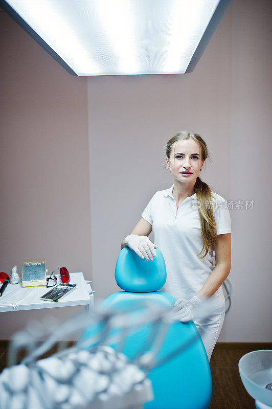好看的女牙医摆姿势在一个现代装备良好的橱柜白大褂。