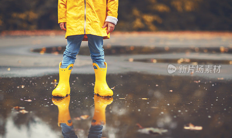 穿着黄色胶靴的孩子的腿在秋天的水坑里
