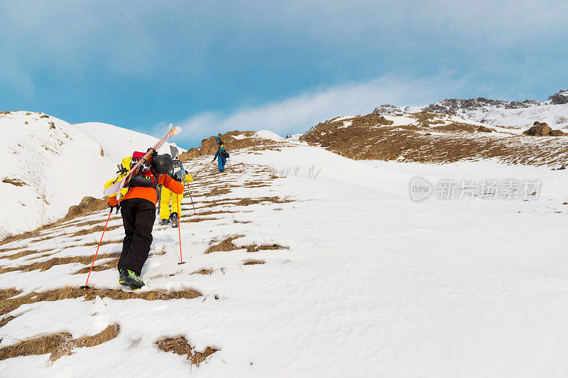 一组三个自由骑手爬上这座山，在荒野的山坡上滑雪