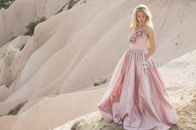 在卡帕多西亚，一名年轻女子穿着粉红色裙子在沙漠中拍照。