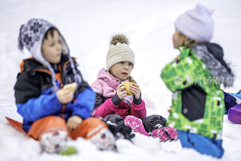 孩子们坐在雪地里吃零食