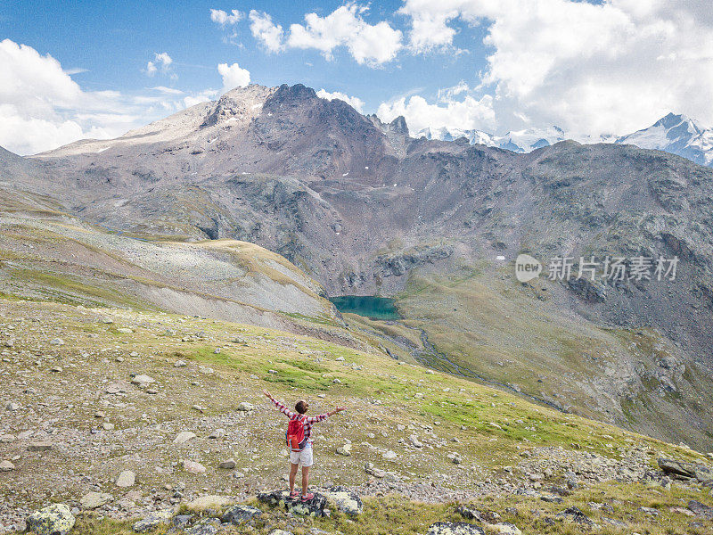 在山顶上徒步旅行的女人站着双臂伸展的无人机视图-在山顶上的成功