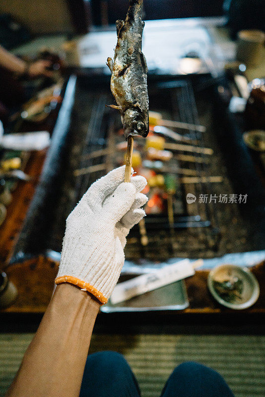 在一家传统的日本餐厅里，一个男人拿着烤鱼