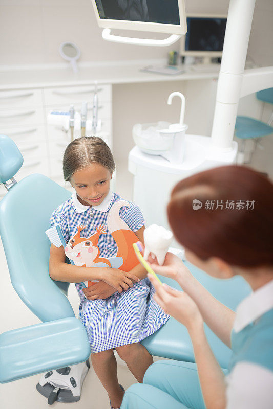 女孩正在听儿童牙医示范如何刷牙