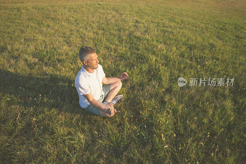 成年人在瑜伽莲花位置冥想在绿色草地上日落