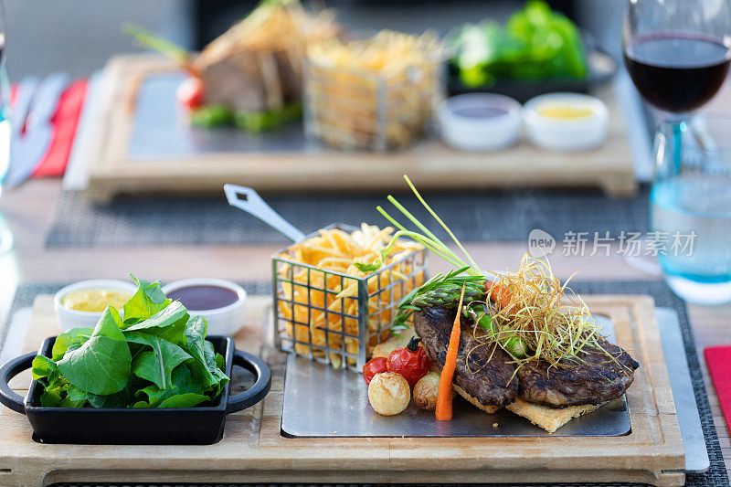 户外餐桌上的烤牛排和土豆片配蔬菜和绿色蔬菜