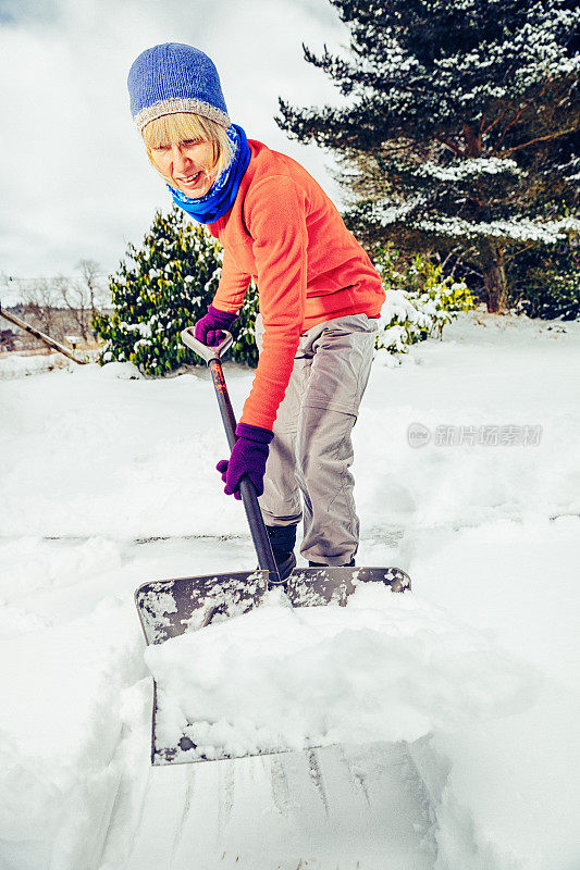 老妇人正在用雪铲清理积雪