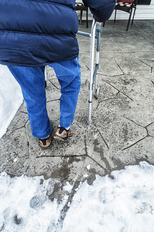 小心翼翼的老人慢慢地推着移动步行者通过雪