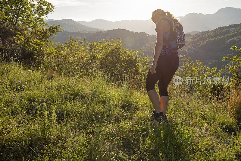 日出时，一名女性徒步旅行者穿过长满青草的山脊