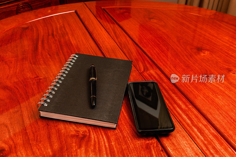 一个笔记本、一支笔和一部手机放在红木桌子上，为商务会议做好准备