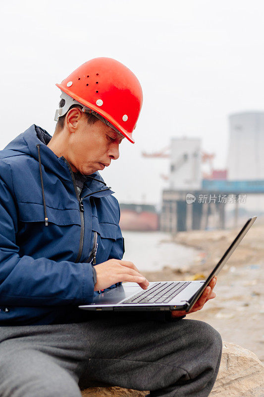 一名男性工程师在码头使用笔记本电脑记录数据并指挥工作