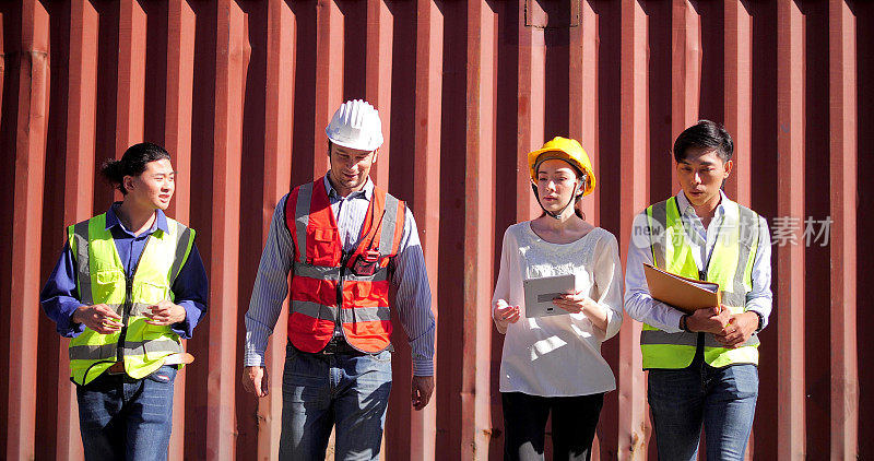 一组工程师工人戴着安全帽在物流集装箱堆场边走边谈