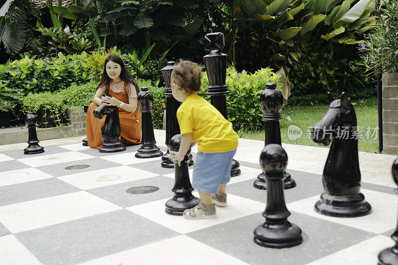 一名亚洲妇女和她的孩子在公园里下巨型国际象棋