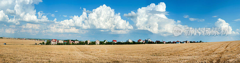 一幅美丽的全景图:修剪过的残茬田，美丽的云朵，地平线上的村庄和房屋