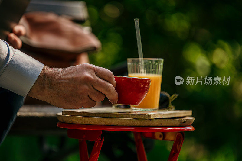 一只男性的手正在从咖啡桌上拿起一个咖啡杯和新鲜的橙汁。
