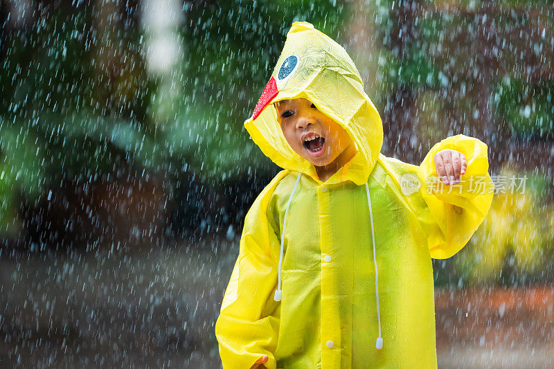 一个穿着雨衣的亚洲男孩在屋外。他在雨中玩耍。