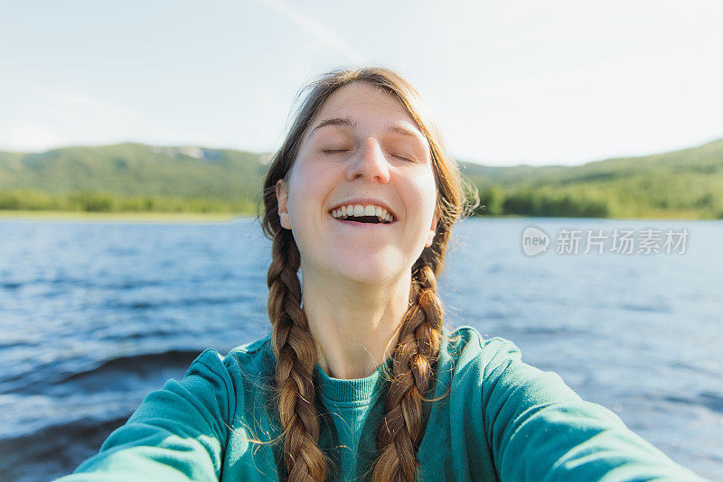 在挪威风景秀丽的湖边，一名梳着辫子的快乐女子自拍